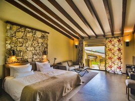 Quarto espaçoso com parede de pedra, uma cama grande, um sofá e vista para o exterior.