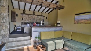 A cozy living area with a sofa, a coffee table, and a kitchen area with a stone wall and wooden beams. - Zornitza Family Estate (Zornitza)
