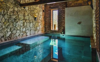 Quarto com paredes de pedra, piscina transparente, janela com vista e parede de tijolos.