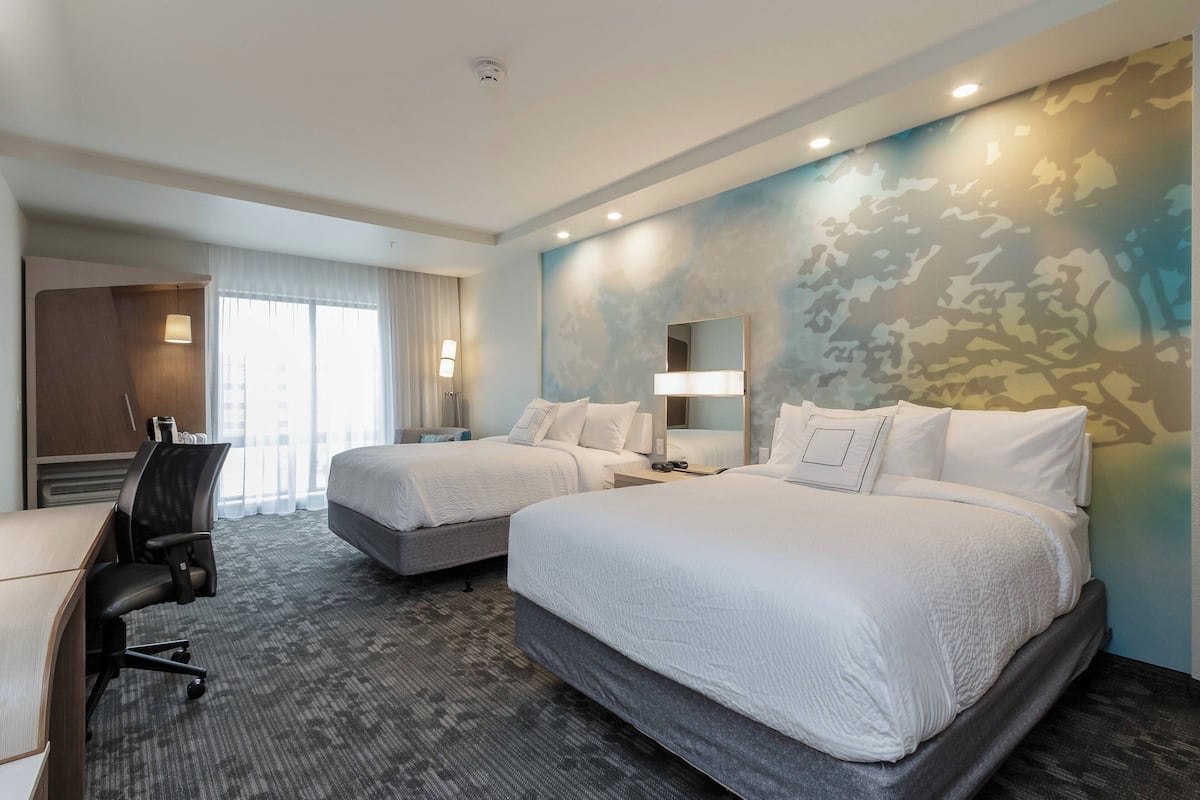 A hotel room with two beds, a desk, and a chair.