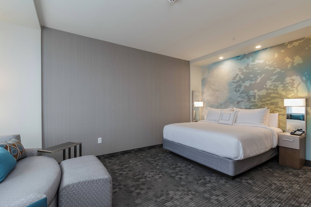 A hotel room with a large bed, a bedside table with a lamp, a small desk, and a couch.
