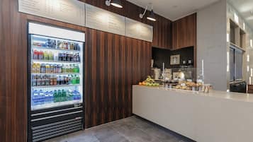 A modern kitchen with a built-in refrigerator stocked with beverages, a coffee machine, and a variety of fresh fruits and pastries.