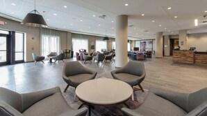 Un vestíbulo amplio con muebles modernos, una recepción y ventanas grandes que dejan entrar luz natural.