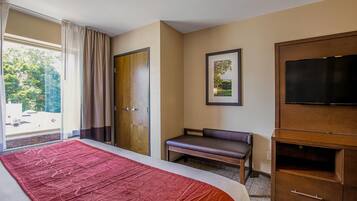 Habitación de hotel con una cama grande, un banco, un televisor y una puerta que da a un balcón.