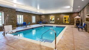 Una piscina interior con pared de piedra, sillas azules y una silla para salvavidas.