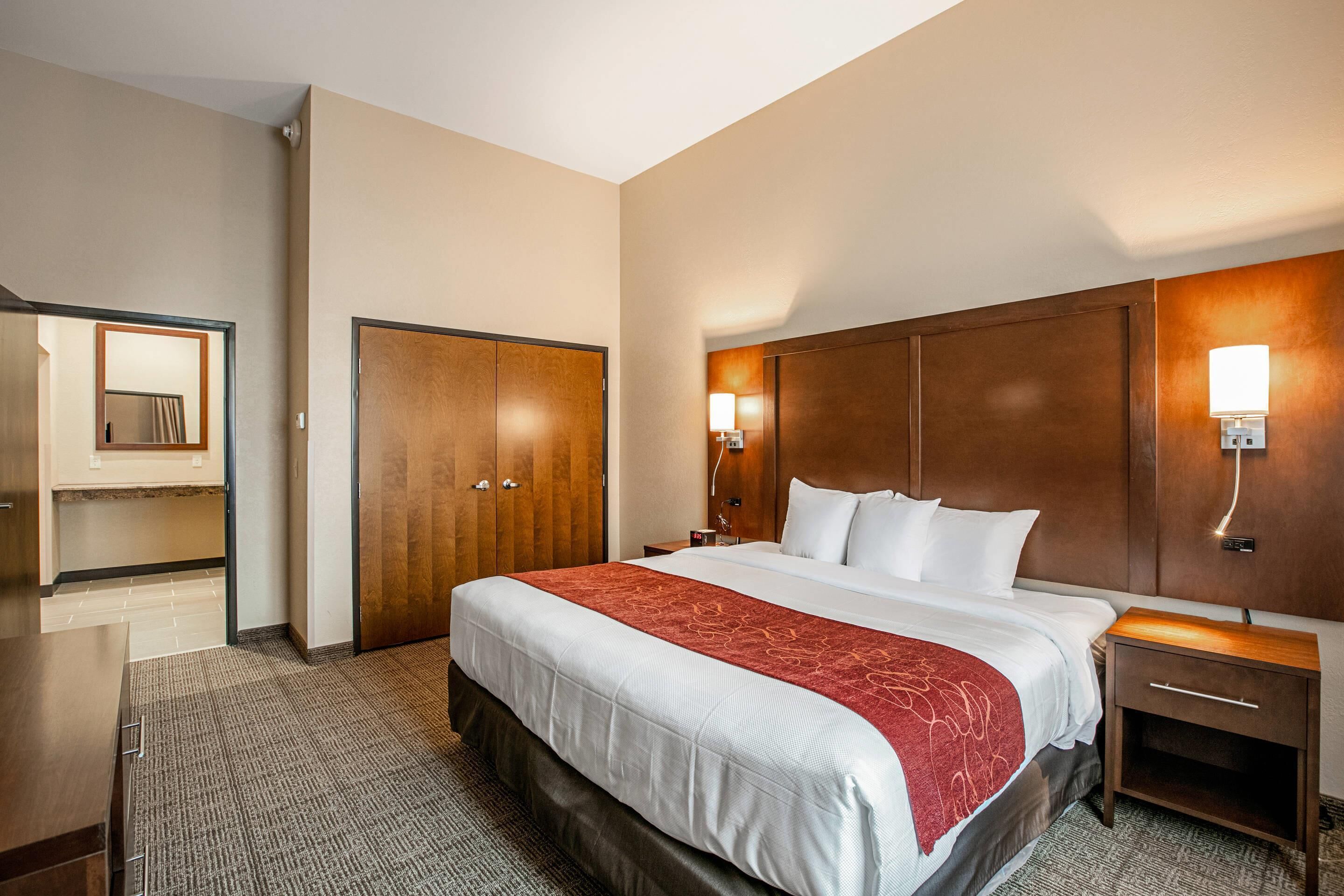 Een hotelkamer met een groot bed, een houten garderobe, een nachtkastje en een spiegel.