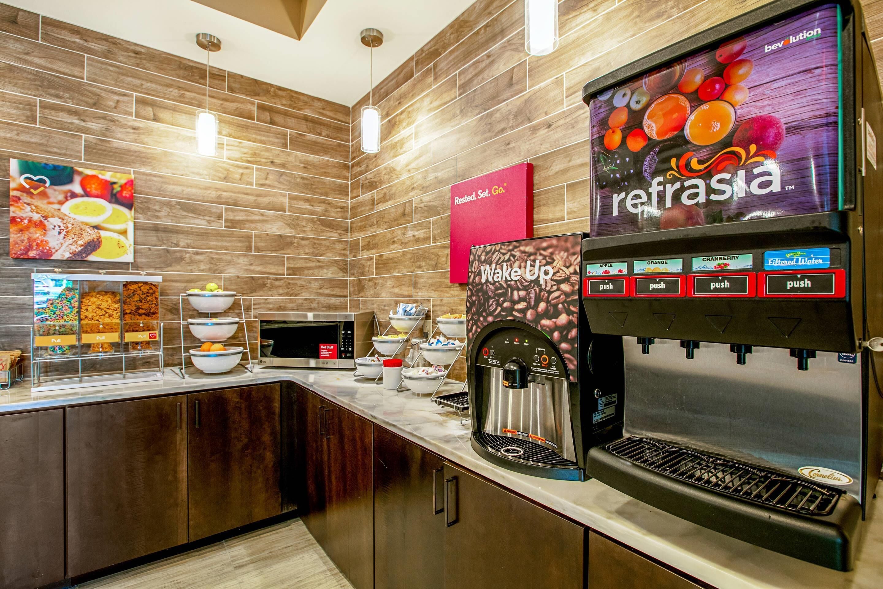 A breakfast bar with a coffee machine, bowls of cereal, and a sign for 'Wake Up'.