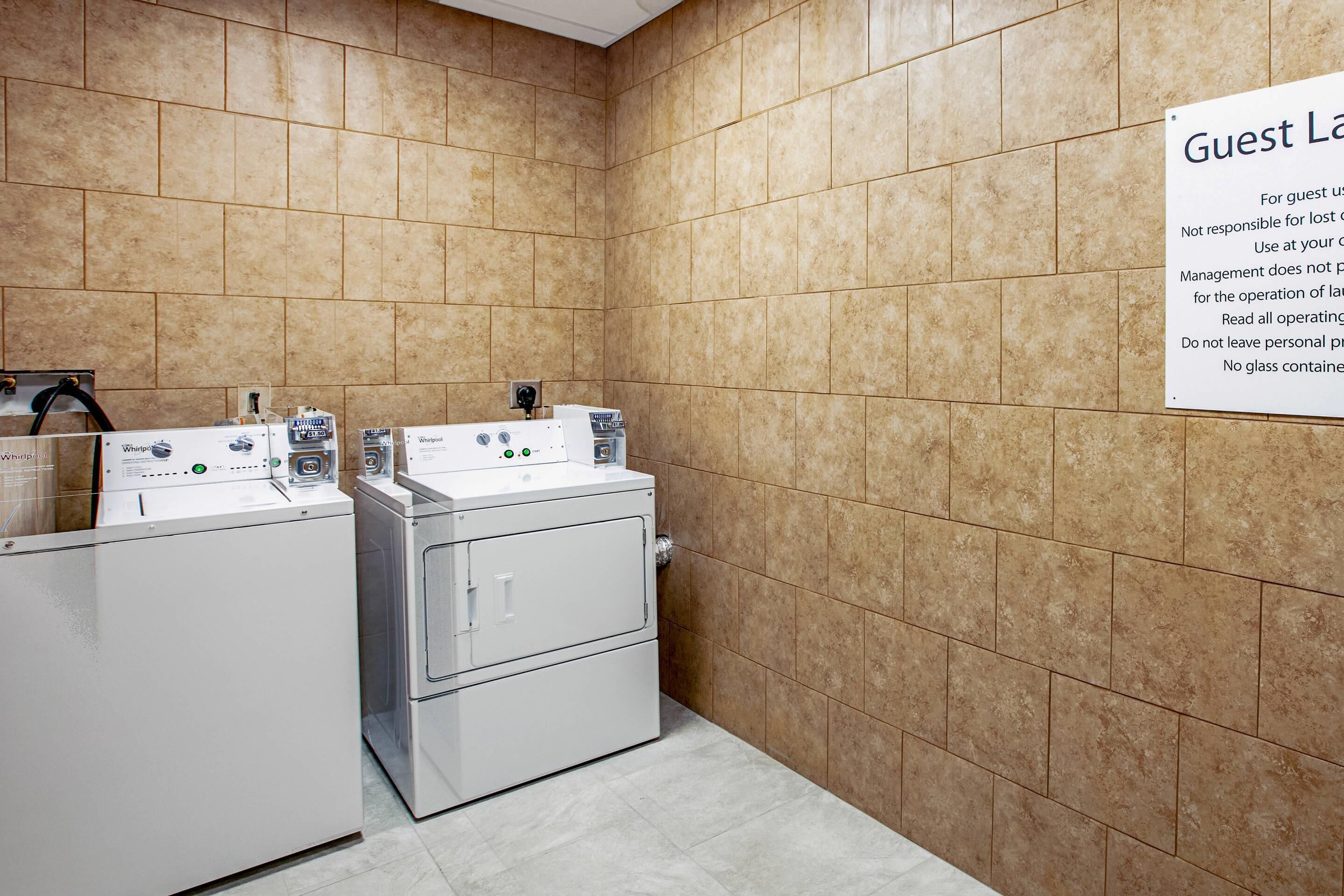 A hotel laundry room with two washing machines and a sign indicating guest laundry services.