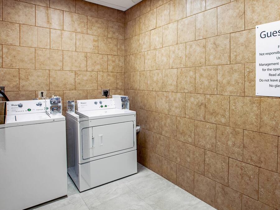 A hotel laundry room with two washing machines and a sign indicating guest laundry services.