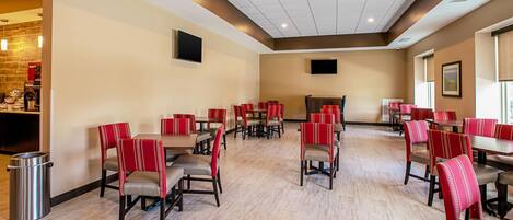 A spacious dining area with multiple tables and chairs, a trash can, and a television mounted on the wall.