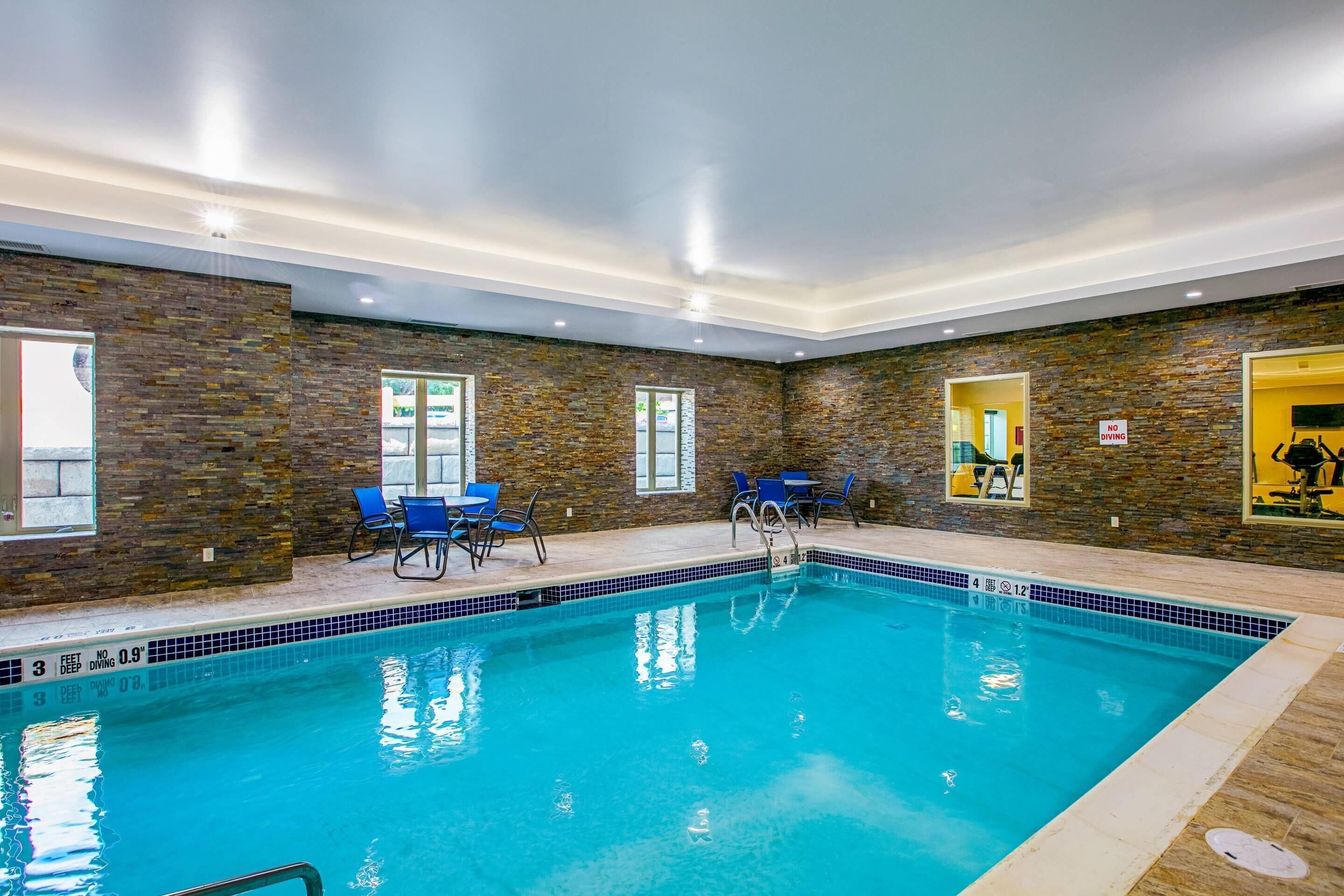 Une piscine intérieure à l’eau claire, entourée de murs en pierre et de chaises bleues.