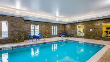 An indoor swimming pool with clear water, surrounded by stone walls and blue chairs.