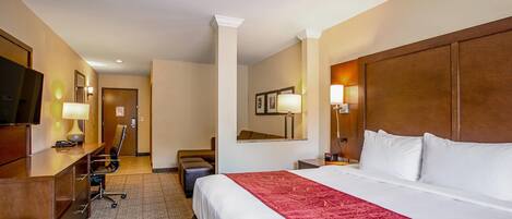 A hotel room with a large bed, a desk, a chair, a television, and a mirror.