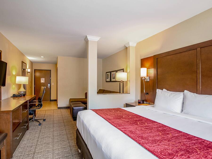 A hotel room with a large bed, a desk, a chair, a television, and a mirror.