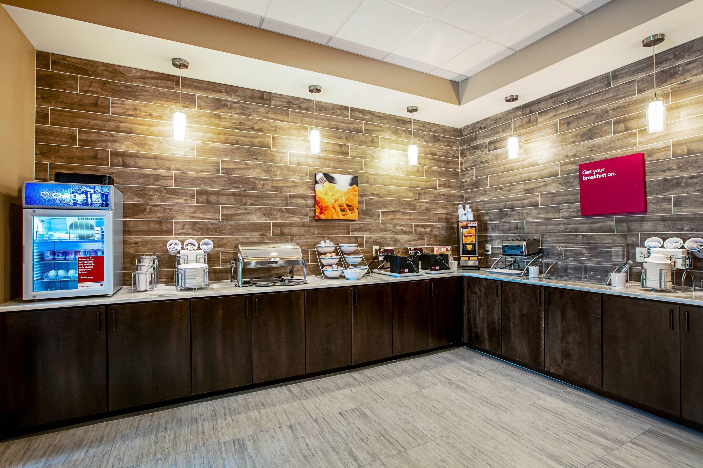 Una barra de desayuno moderna con una exhibición de gofres, una máquina de café y un dispensador de bebidas.