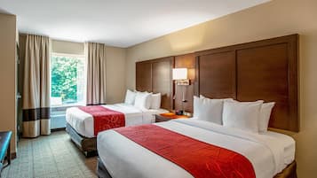 A hotel room with two beds, a desk, and a window with curtains.