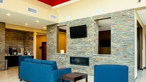 Un área de estar moderna con pared de piedra, televisor de pantalla plana y asientos azules.