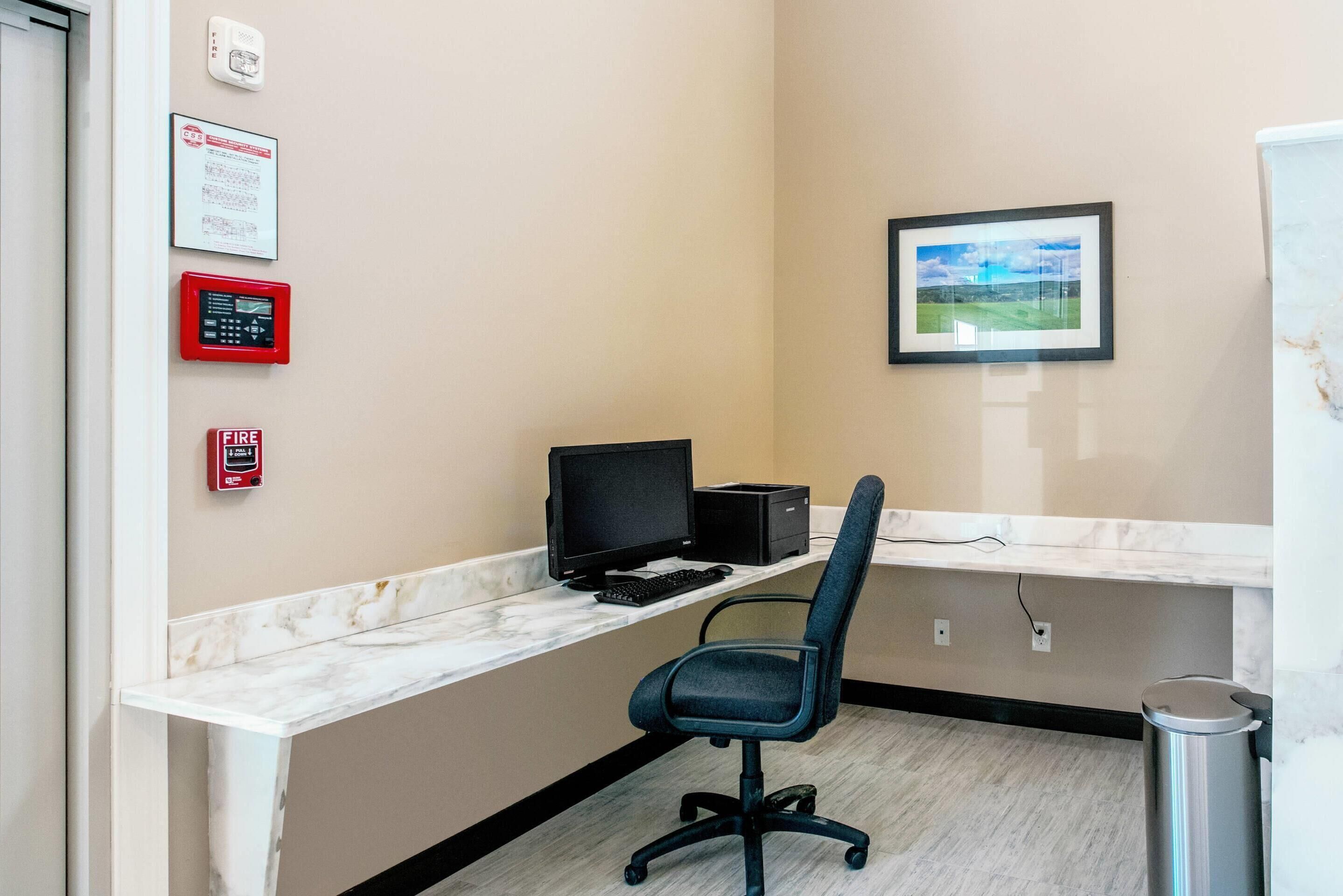 A modern office space with a marble countertop, a black office chair, a computer setup, and a framed landscape picture on the wall.