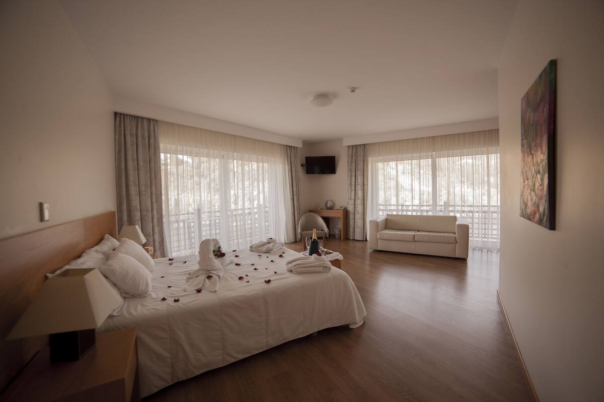 A hotel room with a large bed, a sofa, a TV, and a painting on the wall.