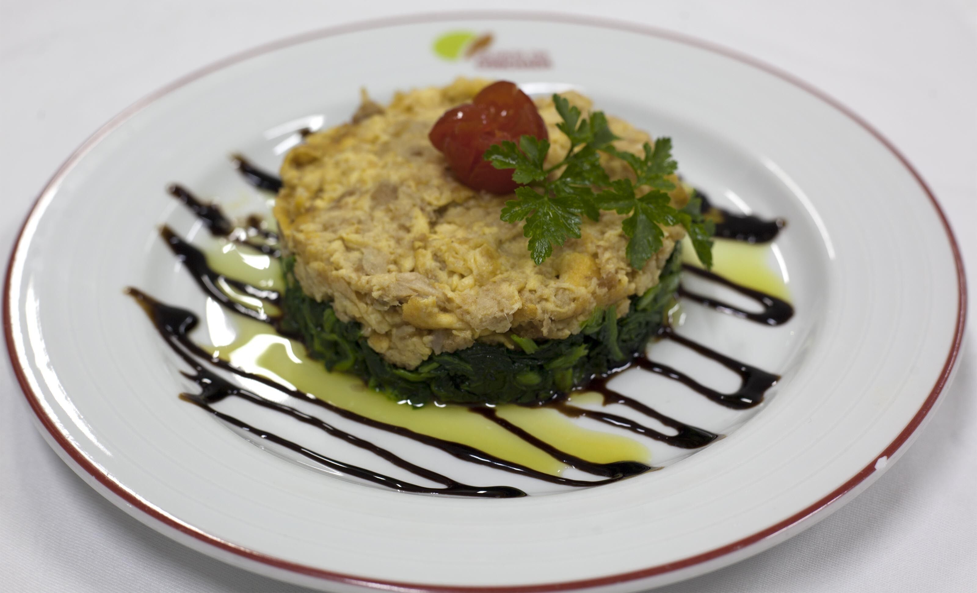 A plate of food with a garnish of parsley and a cherry tomato on top, surrounded by a drizzle of sauce.