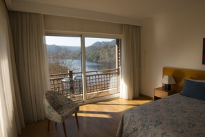 A hotel room with a large window, a bed, a chair, and a nightstand.