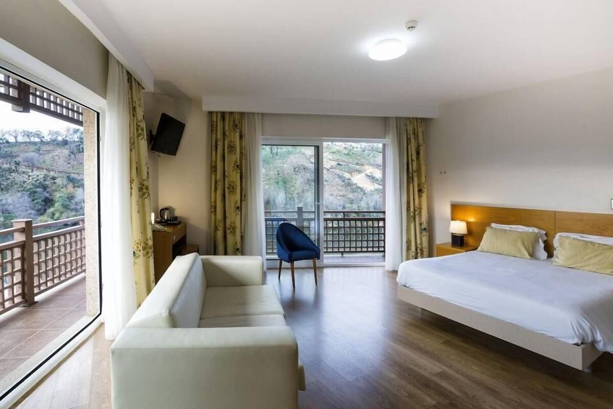 A hotel room with a large bed, a sofa, a chair, and a balcony with a view of the outdoors.