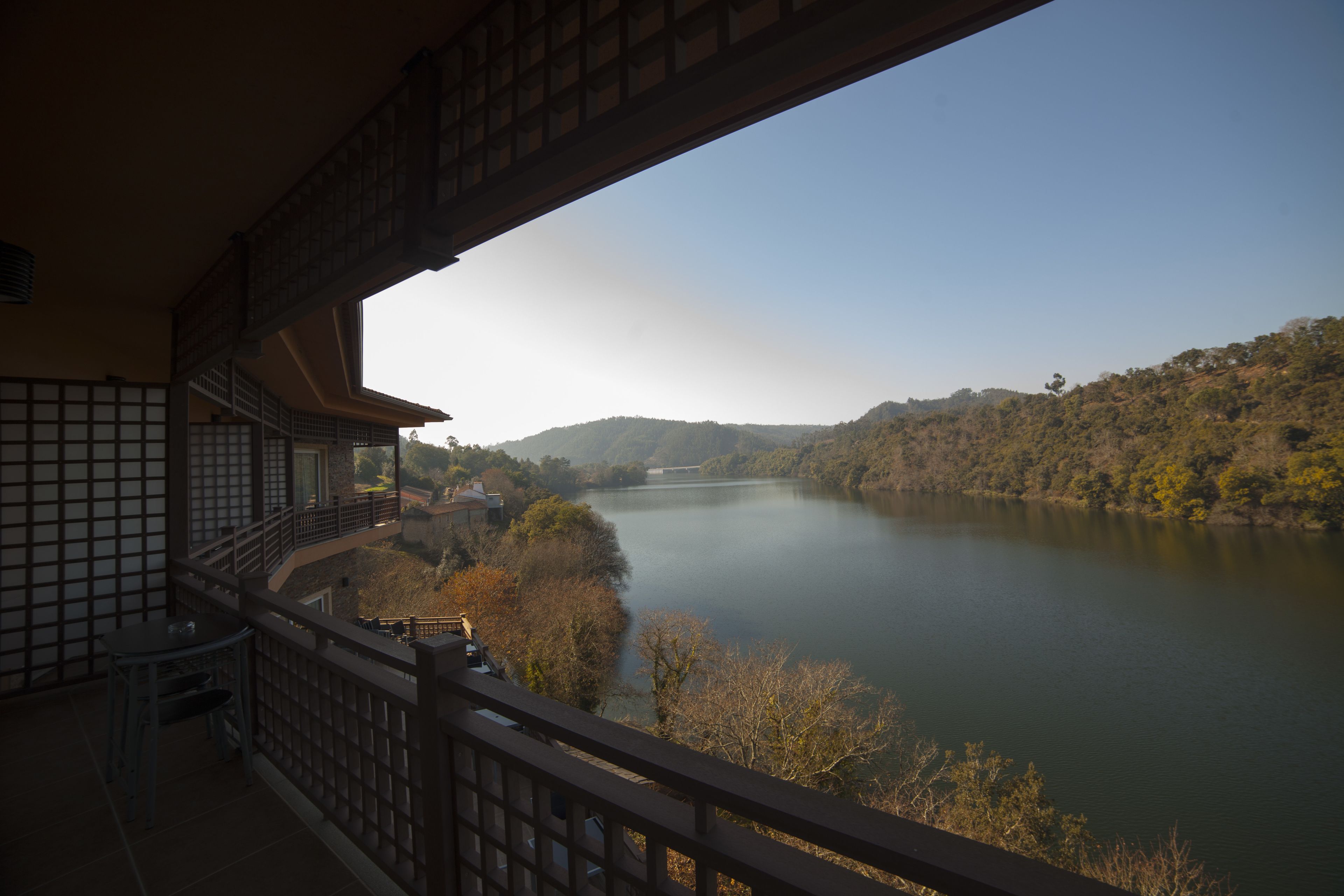A balcony with a view of a calm river and surrounding hills.