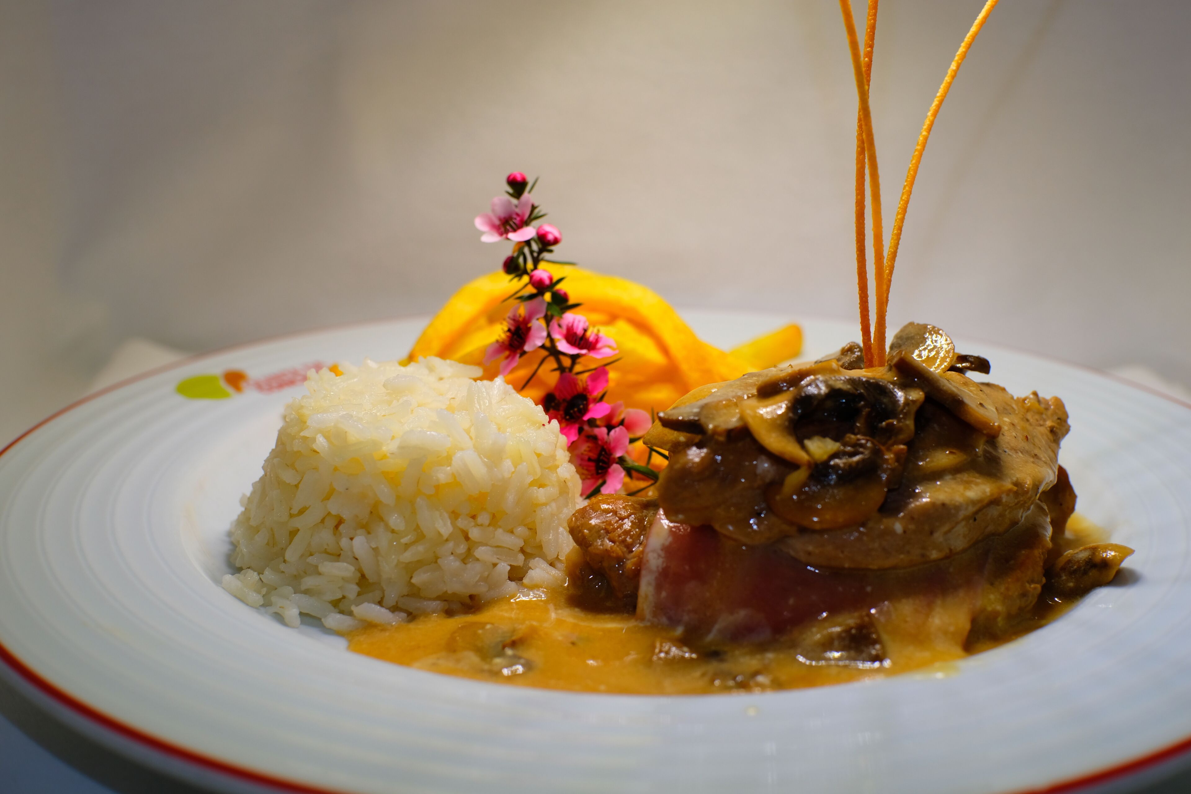 A plate of food with rice and a meat dish, possibly chicken, with a sauce and garnished with flowers.