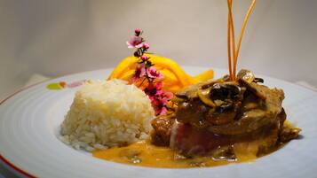 A plate of food with rice and a meat dish, possibly chicken, with a sauce and garnished with flowers.