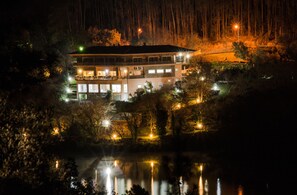 A multi-story building with a reflective pool in front, surrounded by trees and illuminated by streetlights.