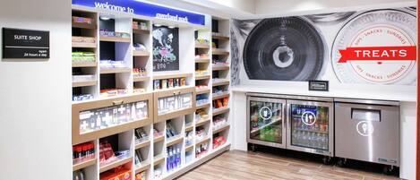 A hotel suite shop with shelves stocked with toiletries and snacks, a welcome sign, and a large wall advertisement for treats.