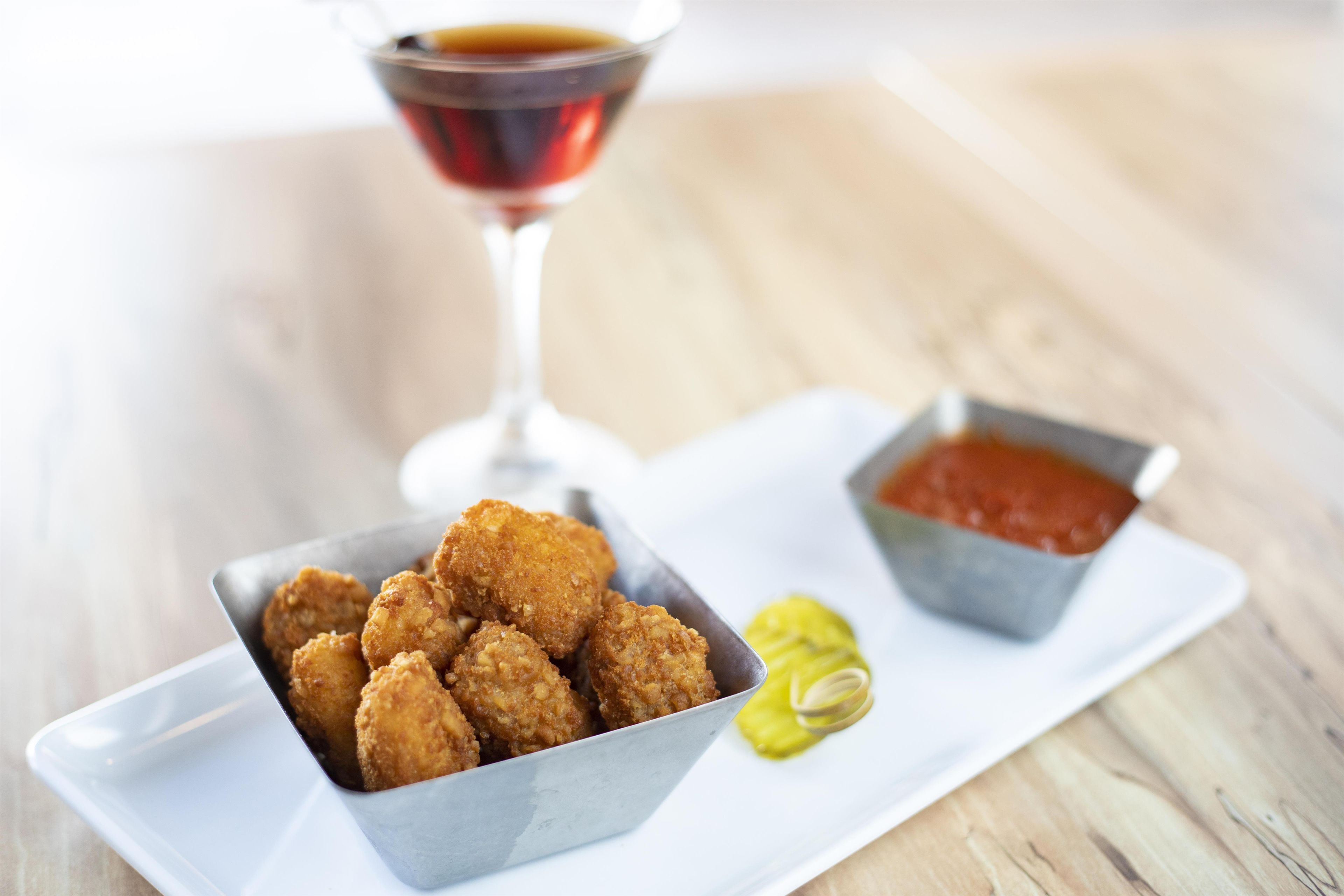A tray with fried food, a glass of red beverage, and a small bowl of sauce on a wooden table.
