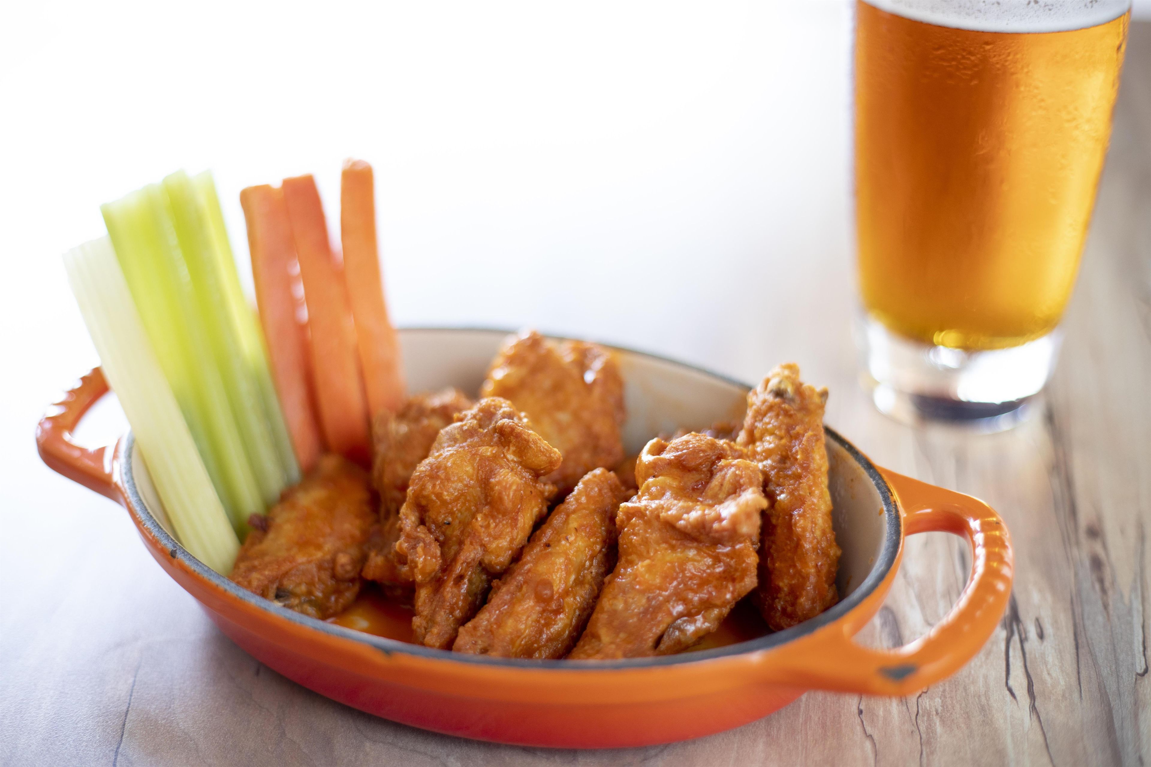 A bowl of chicken wings with celery sticks and a glass of beer.