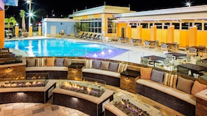 A poolside area with a fire pit, lounge chairs, and a seating area with cushions.