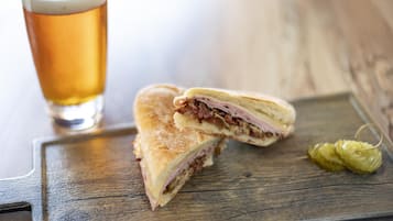 A sandwich cut in half, a glass of beer, and a pickle on a wooden table.