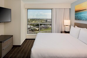 Habitación de hotel con una cama grande, un televisor de pantalla plana, un ventanal con vistas a la ciudad y un cuadro en la pared.