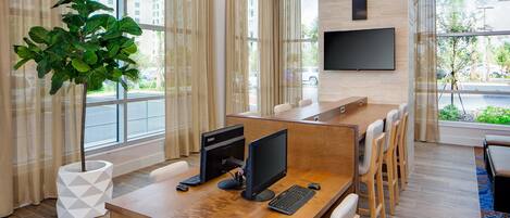 Una sala de conferencias moderna con una mesa de madera, dos monitores y una planta grande en maceta.