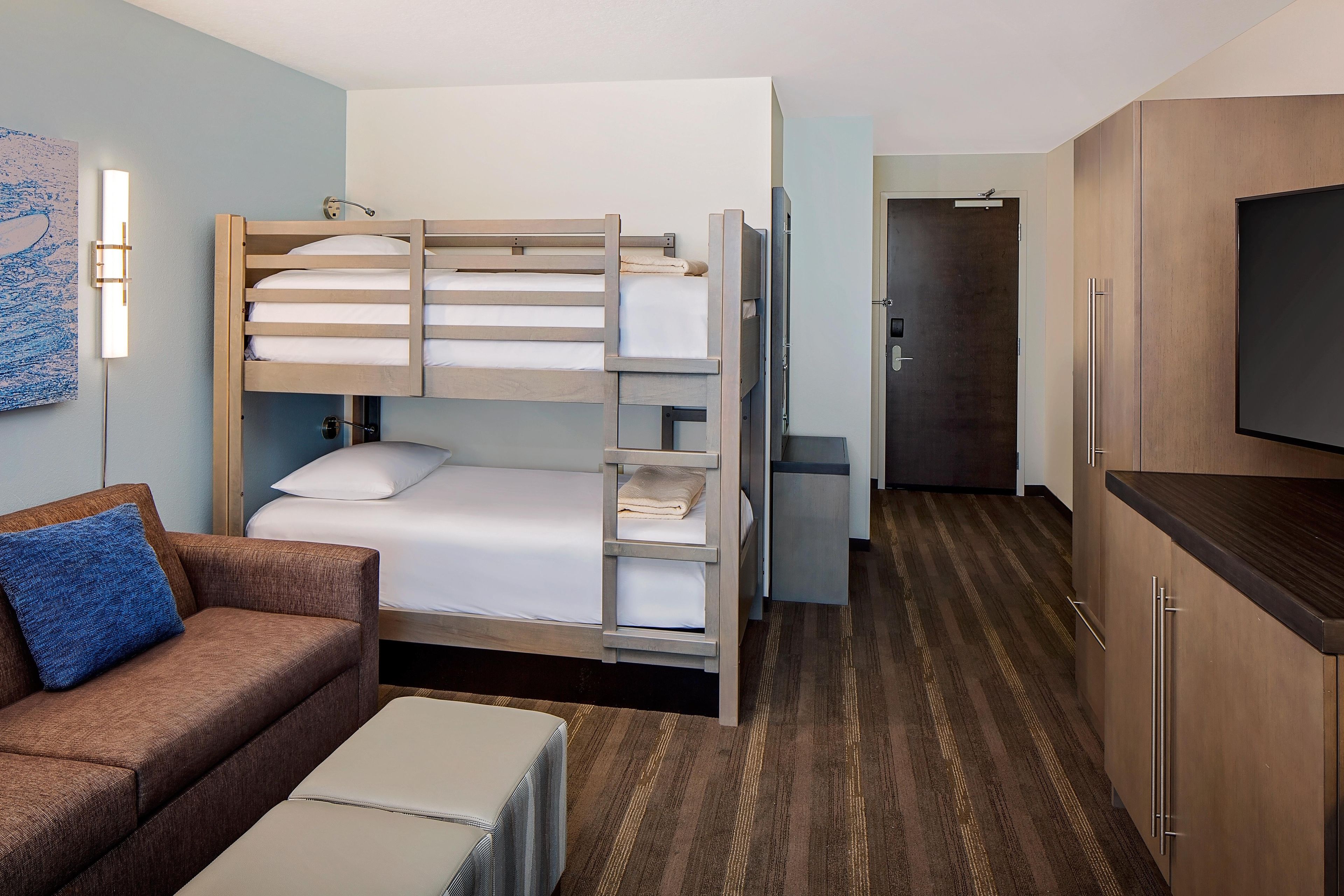 Ein Hotelzimmer mit Etagenbett, einer Schlafcouch, einem Fernseher und einer Küchenzeile.