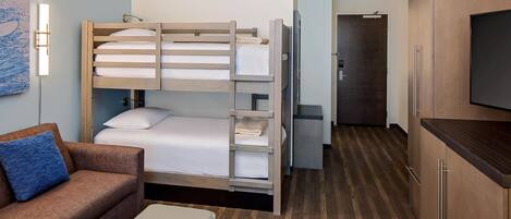 Ein Hotelzimmer mit Etagenbett, einer Schlafcouch, einem Fernseher und einer Küchenzeile.