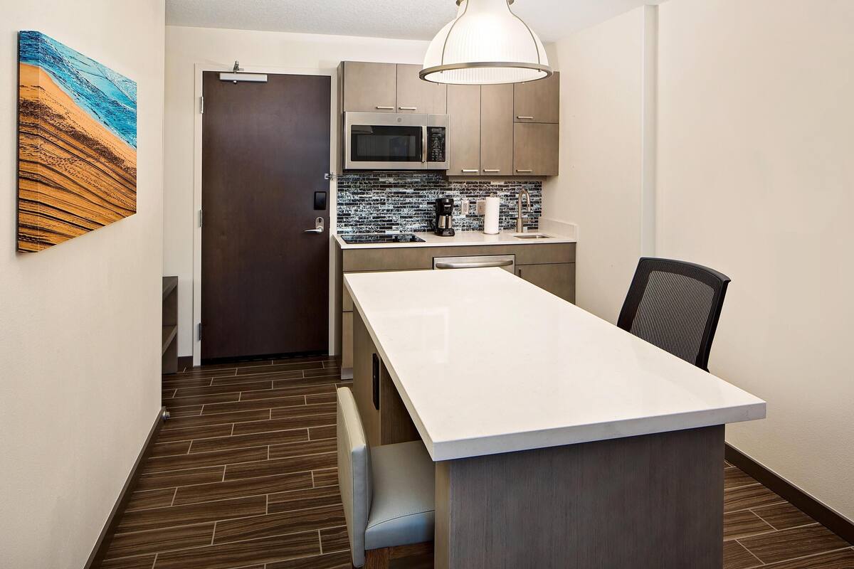 A modern kitchen with a white countertop, stainless steel microwave, and a hanging light fixture.
