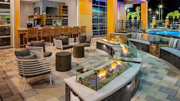 A well-lit outdoor lounge area with seating, a bar, and a pool.