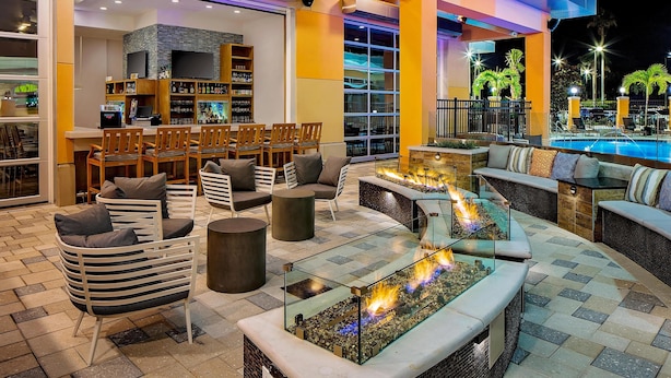 A well-lit outdoor lounge area with seating, a bar, and a pool view.