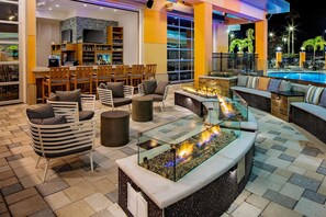 Un área de descanso al aire libre bien iluminada con asientos, un bar y vista a la piscina.