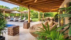 A covered outdoor area with lounge chairs, a pool, and potted plants.