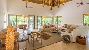 A spacious living area with a high ceiling, large windows, and a thatched roof.