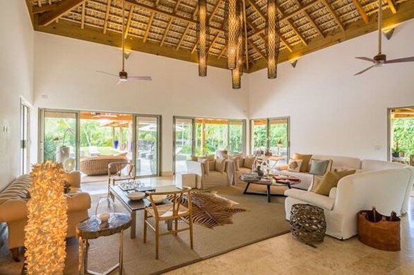 A spacious living area with a high ceiling, large windows, and a thatched roof.