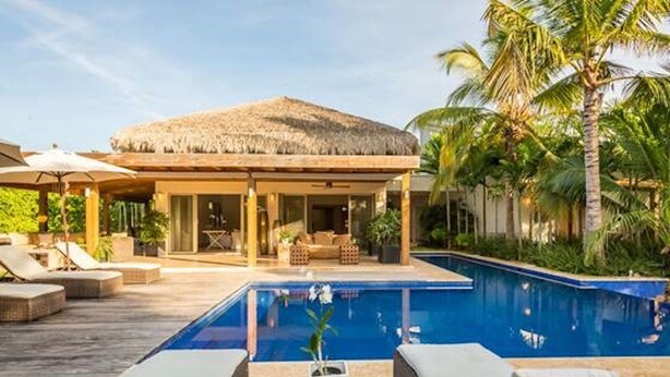 A poolside area with lounge chairs, a thatched-roof structure, and a clear blue pool.