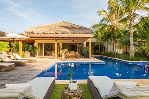A poolside area with lounge chairs, a thatched-roof structure, and a clear blue pool.