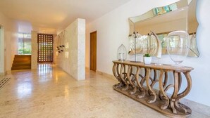 A spacious hallway with a marble floor, a wooden console table with glassware, and a large mirror on the wall.