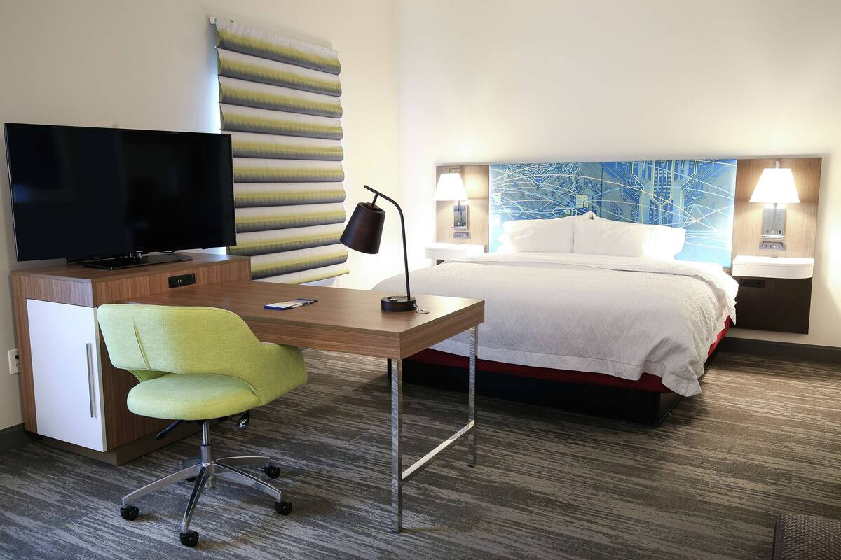 A hotel room with a bed, a desk with a chair, a television, and two bedside lamps.